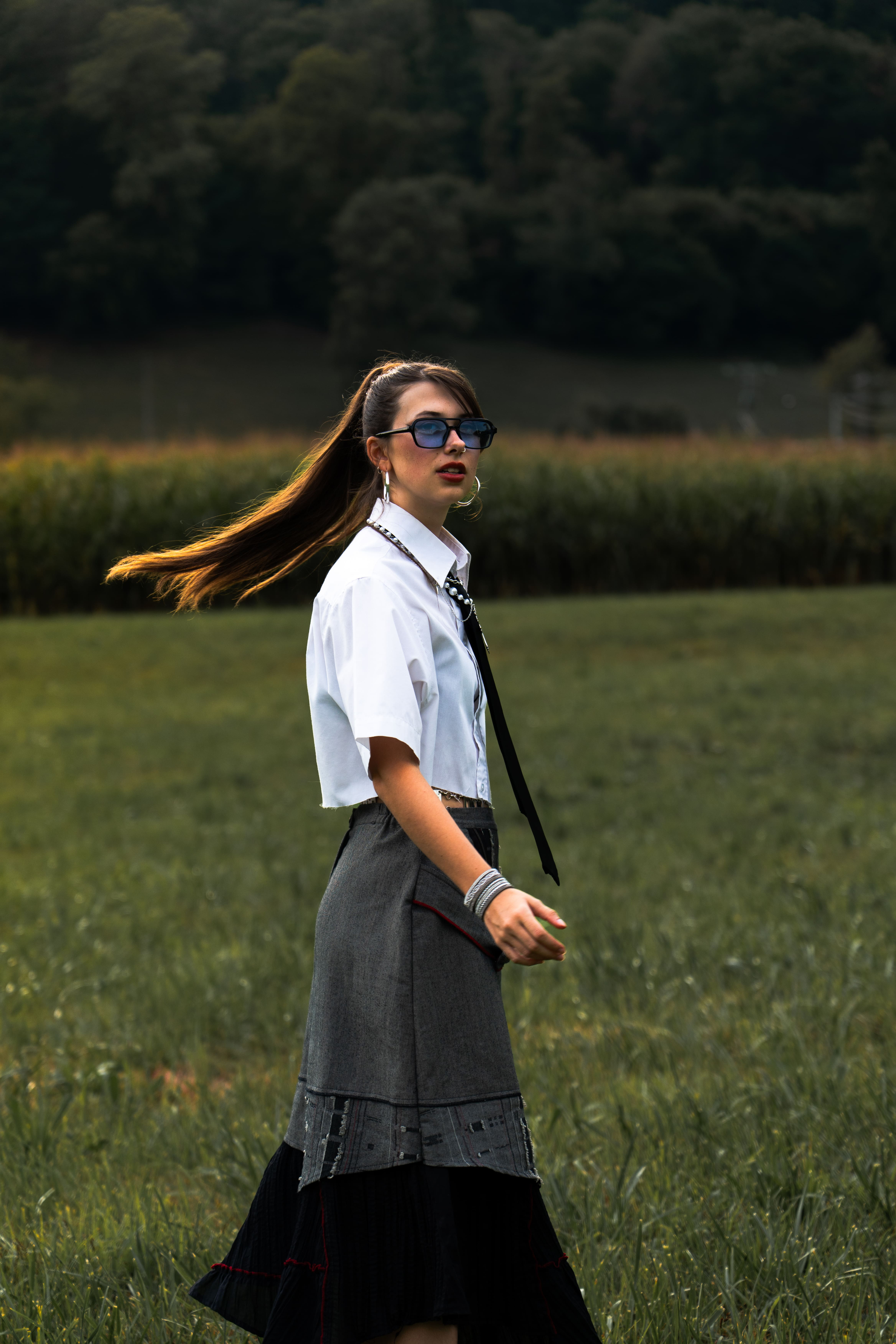 photographie femme dans un champs qui se tourne corps en mouvement cheveux au vent en queue de cheal bien habillée jupe grise et chemise blanche photographge de mode chambéry grenoble