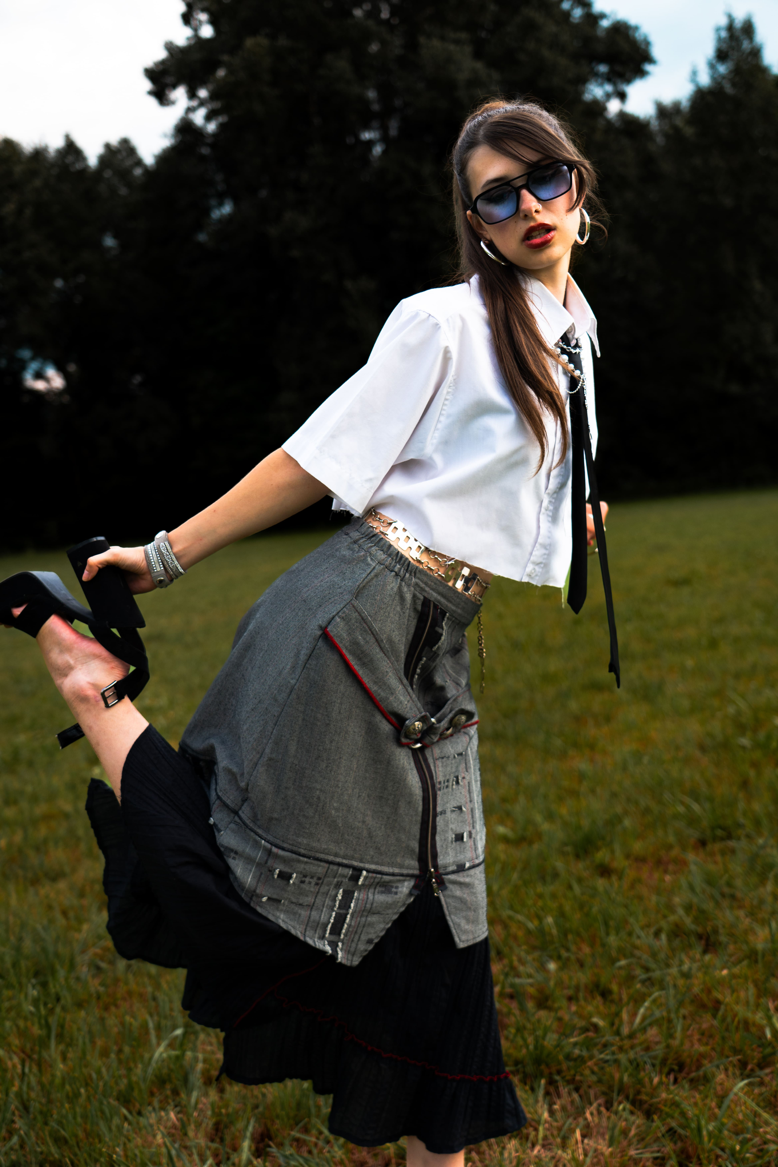 photo femme mode en jupe chemise blanche cravate lunette de soleil cheveux noirs longs en queue de cheval dans un champ au flash