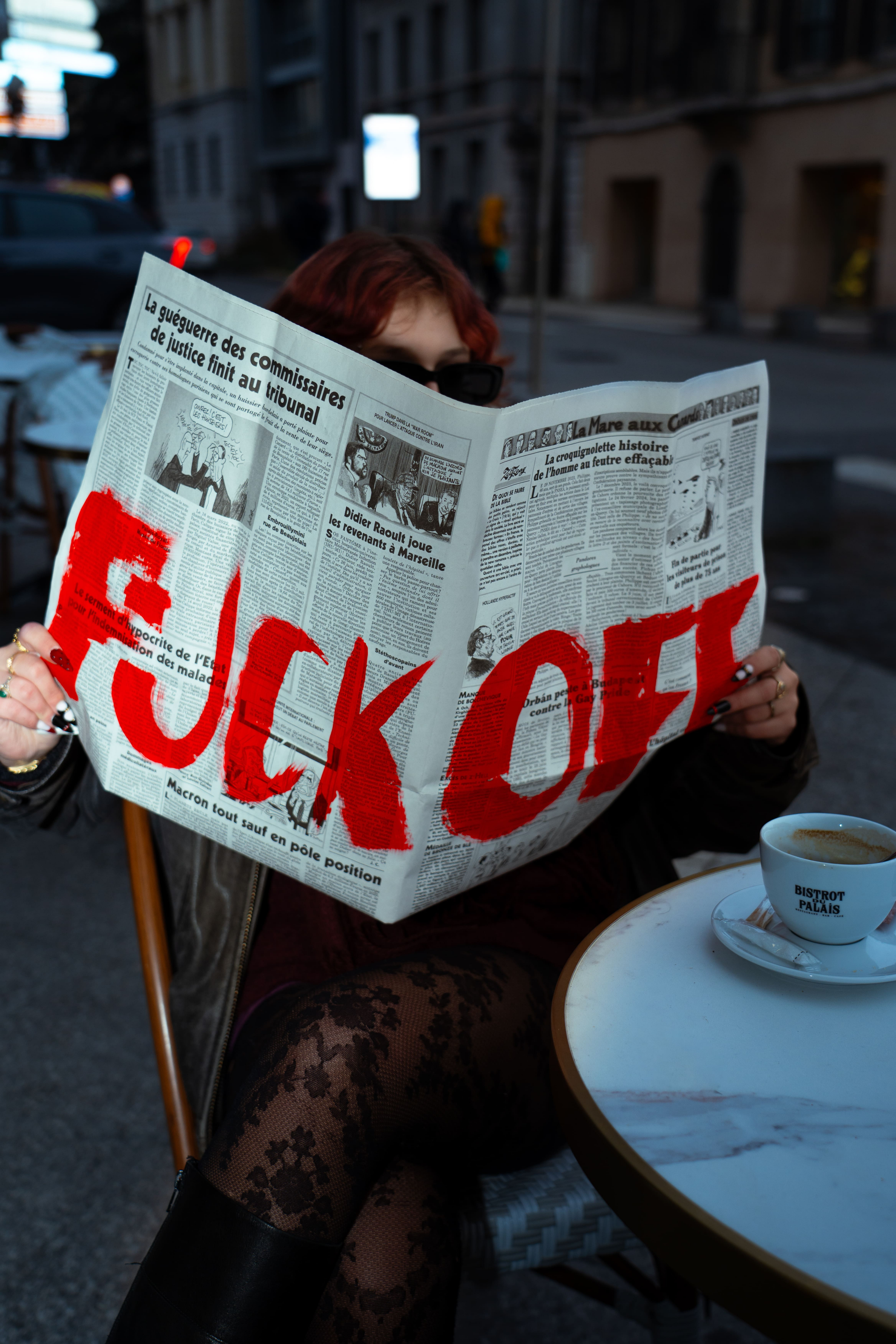 Femme assise en terasse à une table avec un journal sur lequel il écrit FUCK OFF. Création originale de Pauline artbook photographge de mode chambéry grenoble