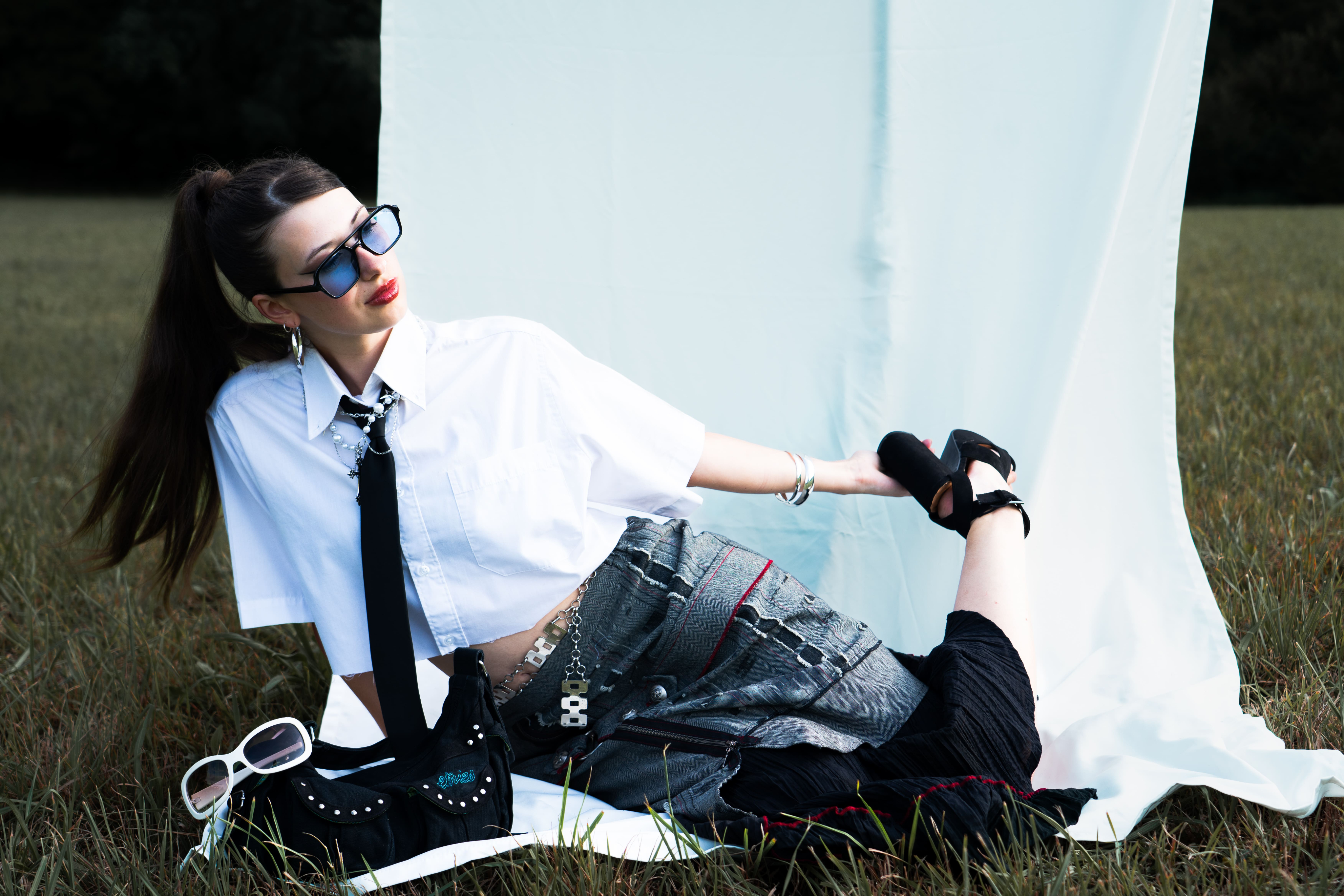 femme allongée qans un champs devant un drap blanc habillée en jupe talons chemise blanche cravate cheveux longs noirs en queue de cheval photographe de mode chambéry grenoble