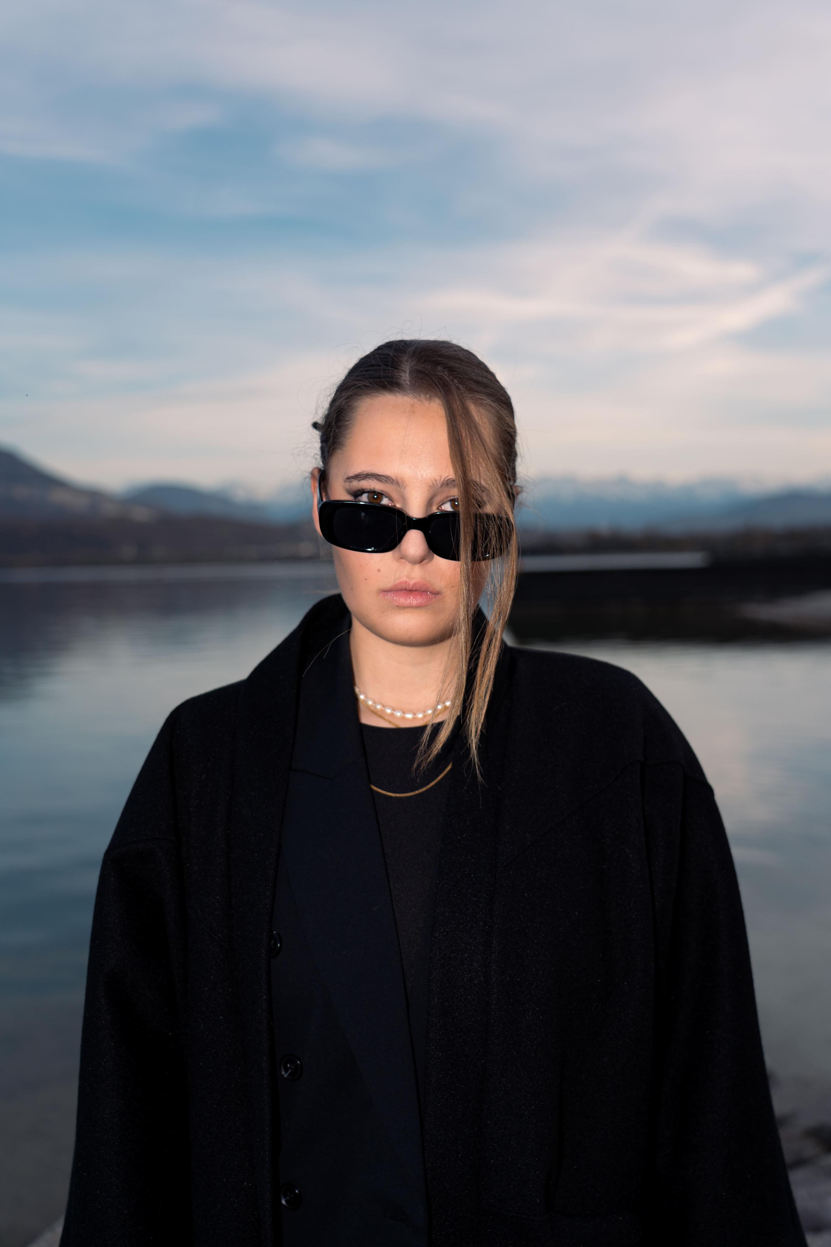 photo femme blonde devant le lac du bourget. Habillée en noir et avec des lunettes de soleil noires photographge de mode chambéry grenoble