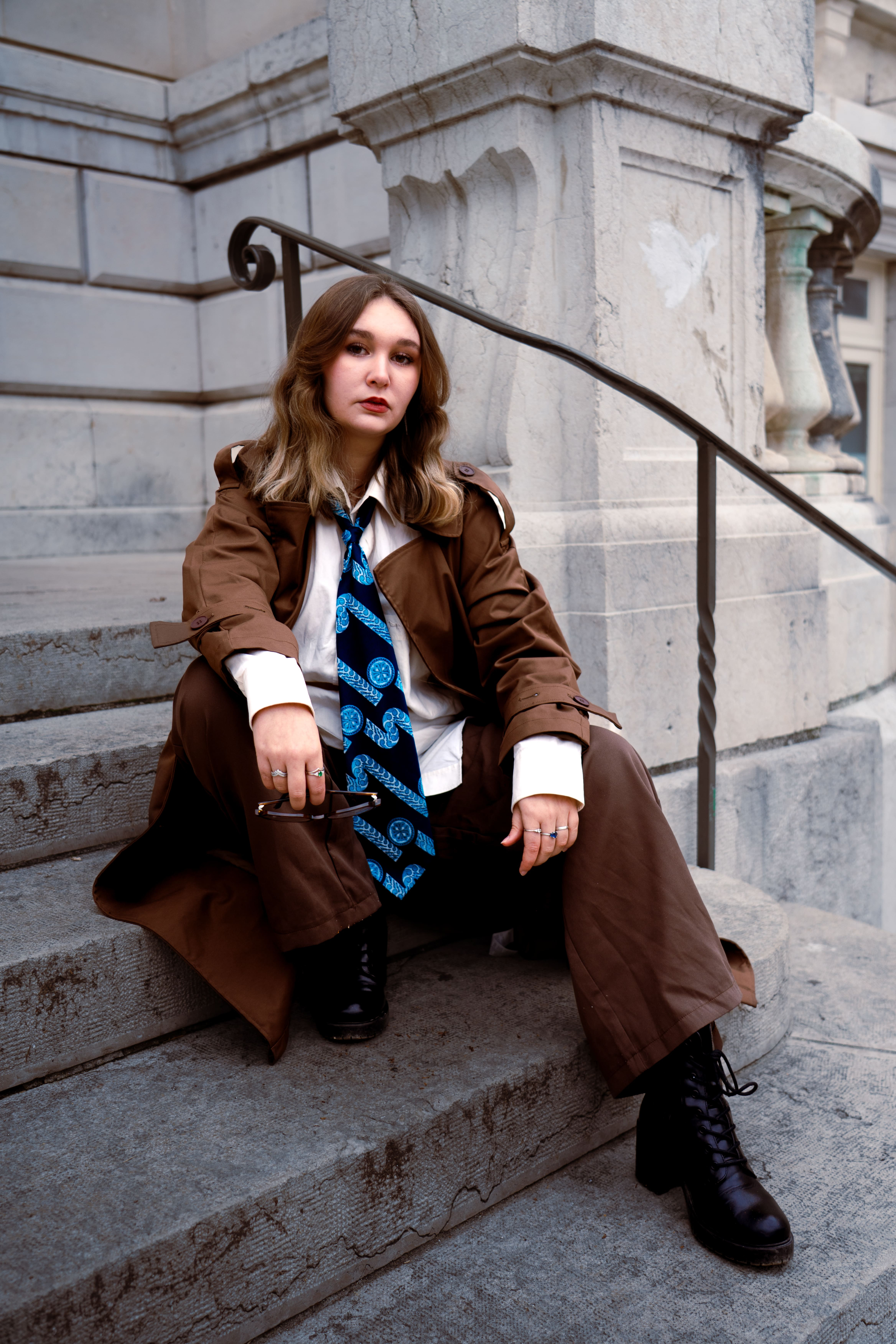 photo mode femme assise sur des escaliers en ville dans un costume et une veste marron avec une chemise blanche et une cravate bleue. Business woman blonde et jeune photographge de mode chambéry grenoble