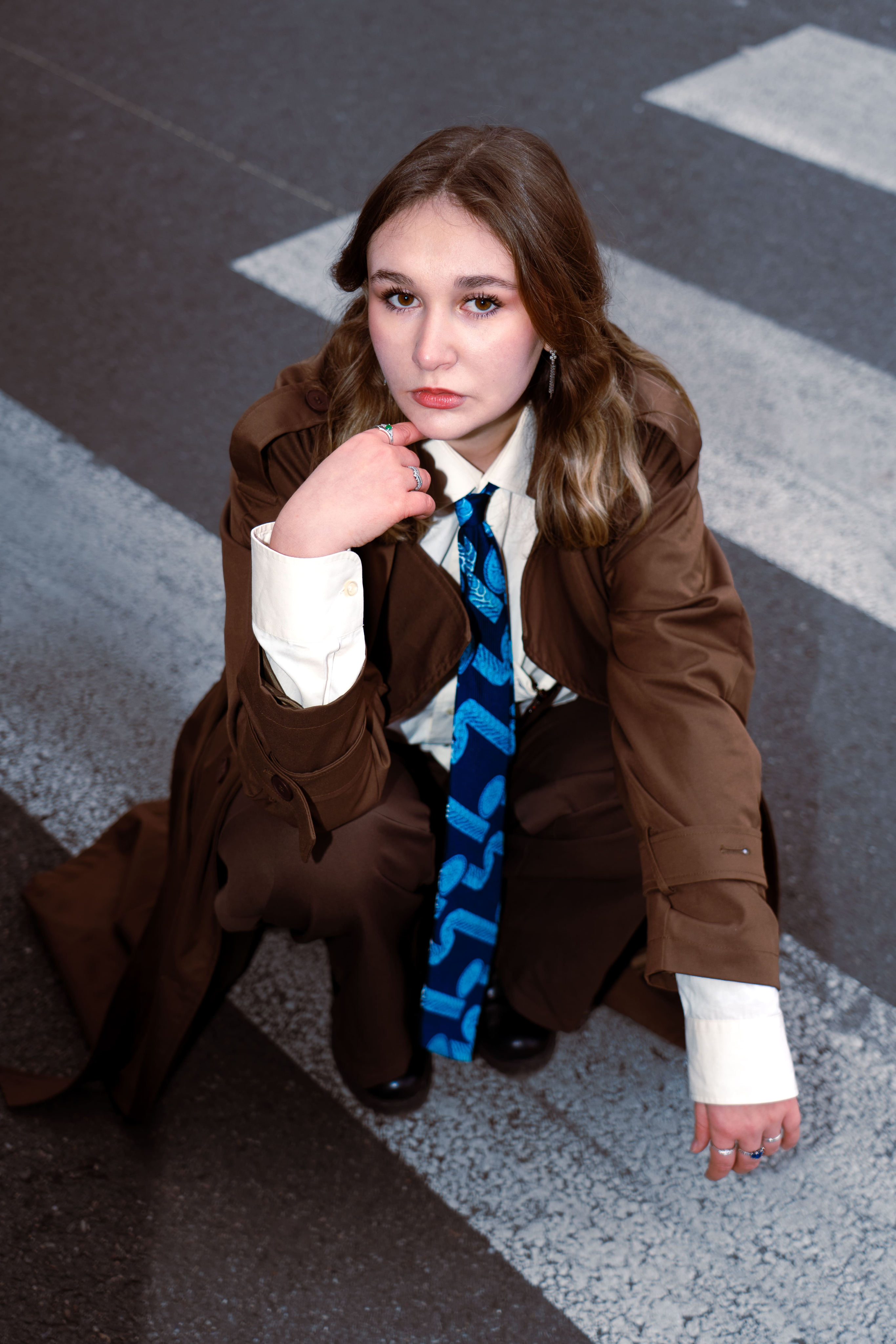 photo femme accroupie sur un passage piéton en angle de vue plongée avec un costume et une veste marron et une chemise blanche avec une ccravate bleue. Femme blonde jeune photographge de mode chambéry grenoble