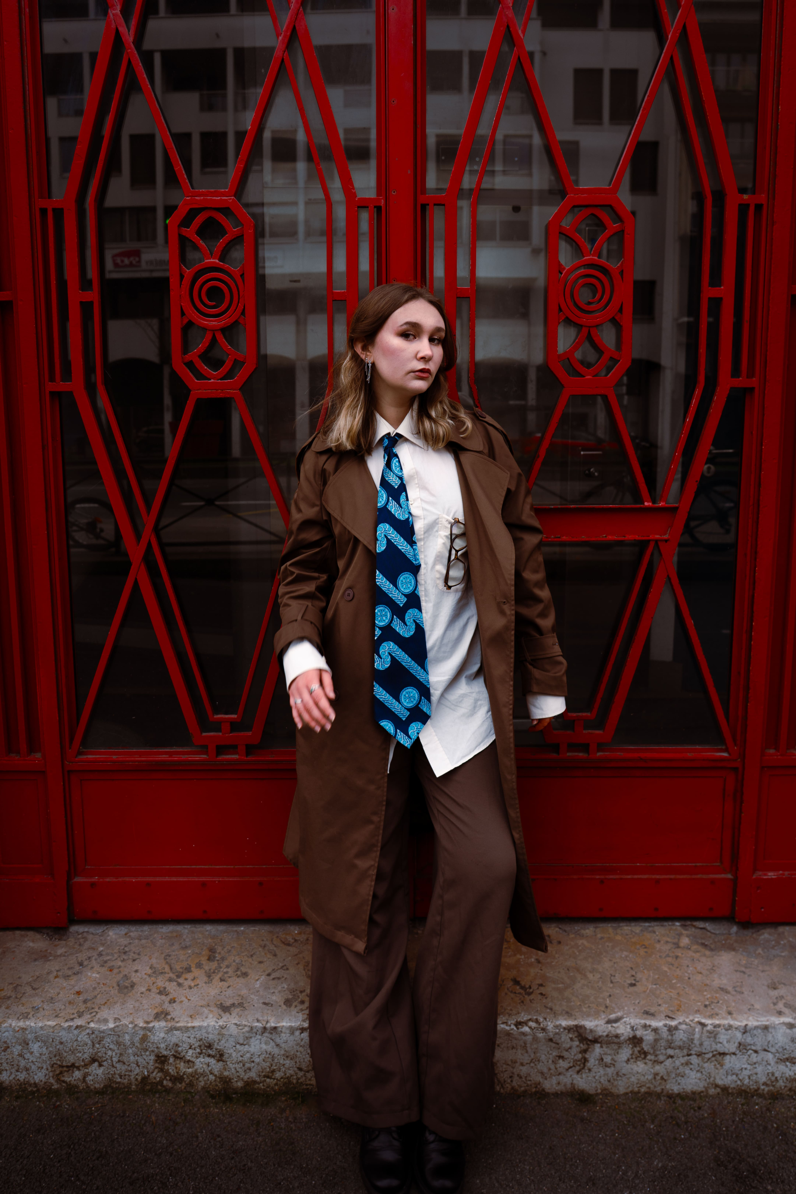 femme blonde business woman adossée contre une porte métallique rouge en costume marron avec chemise blanche et cravate bleue photographge de mode chambéry grenoble